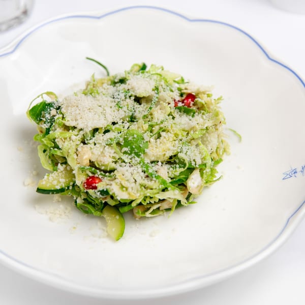 Shredded Brussels sprout salad with parmesan cheese and pomegranate seeds on a white scalloped plate.