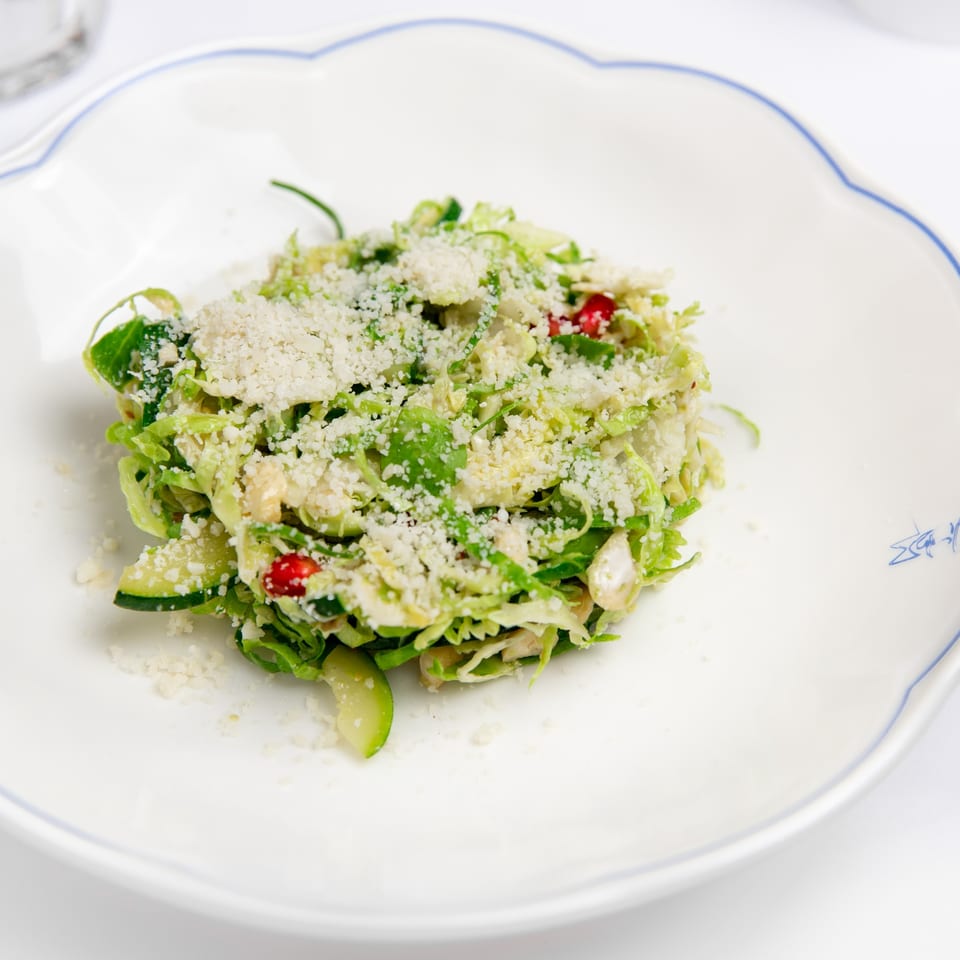 Shredded Brussels sprout salad with parmesan cheese and pomegranate seeds on a white scalloped plate.