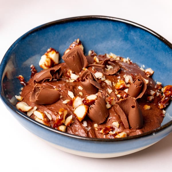 Rich chocolate mousse with chocolate shavings and chopped nuts in a blue bowl.