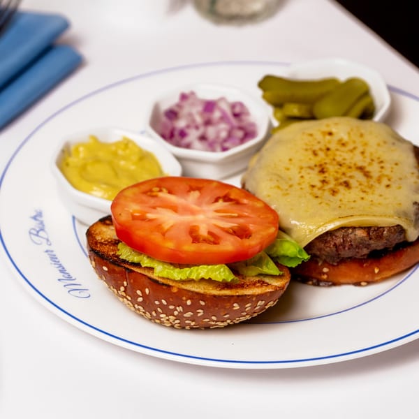 Monsieur Bistro burger with melted cheese, lettuce, tomato, and sides of mustard, onions, and pickles.