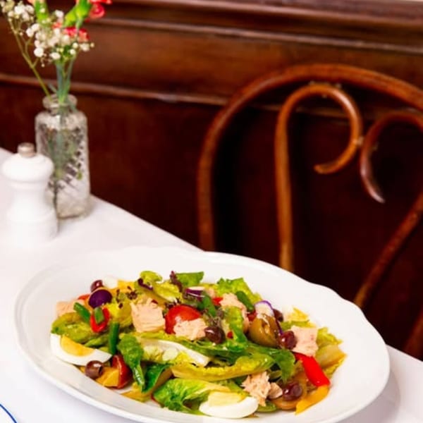 A vibrant Salade Niçoise with tuna, eggs, olives, and vegetables on a white table at Monsieur Bistro.