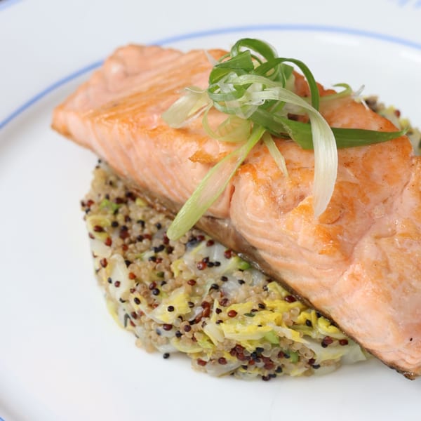 Pan-seared salmon fillet topped with scallions, served over a bed of quinoa and cabbage.