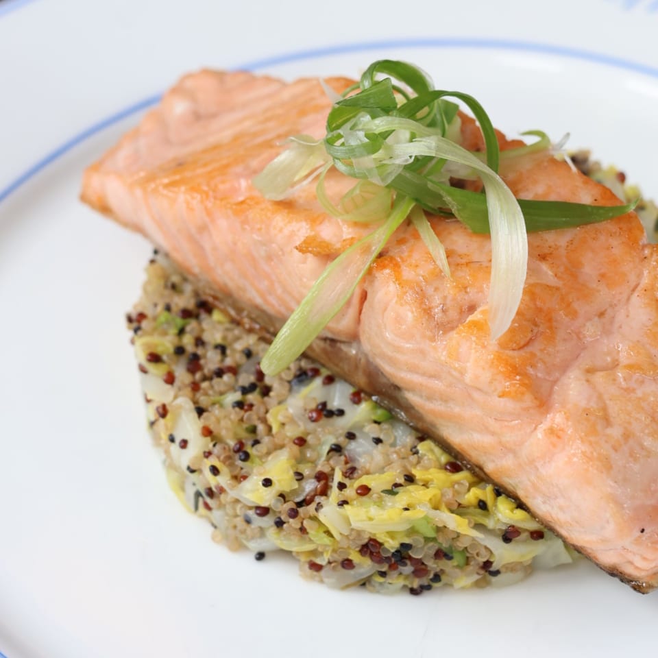 Pan-seared salmon fillet topped with scallions, served over a bed of quinoa and cabbage.