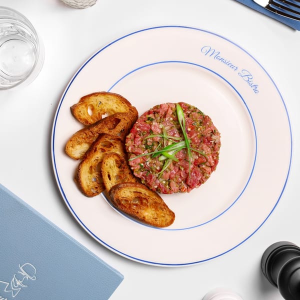 Monsieur Bistro's steak tartare with toasted bread on a white plate with blue trim.