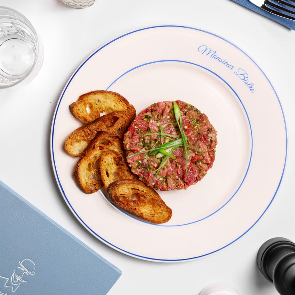 Monsieur Bistro's steak tartare with toasted bread on a white plate with blue trim.
