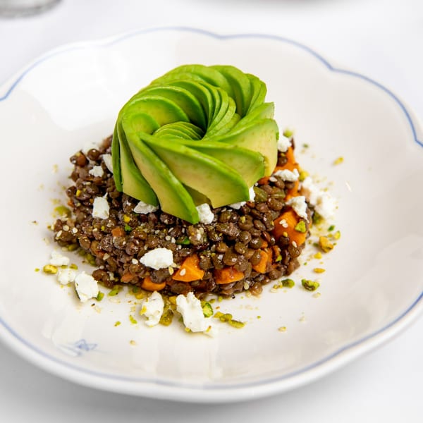 Lentil and sweet potato salad topped with fanned avocado, feta, and pistachios on a white plate.